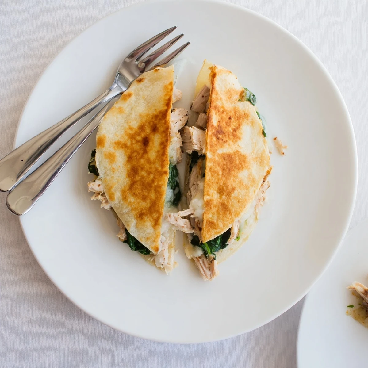 A golden, crispy Chicken and Spinach Quesadilla topped with fresh cilantro and sour cream on a rustic plate.