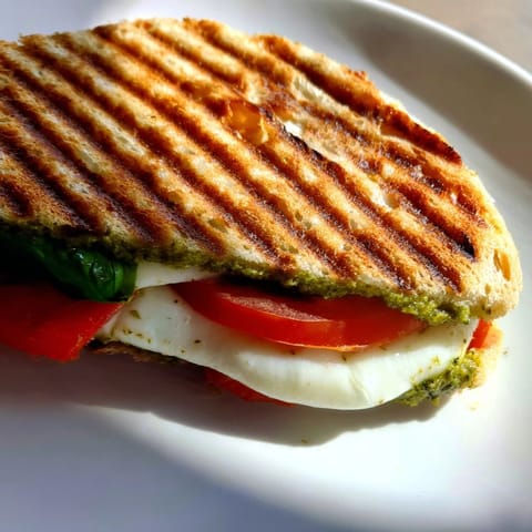 Golden-brown Panini Press Innovations sandwich with melted mozzarella, fresh tomato slices, and basil leaves, pressed on a wooden board.  