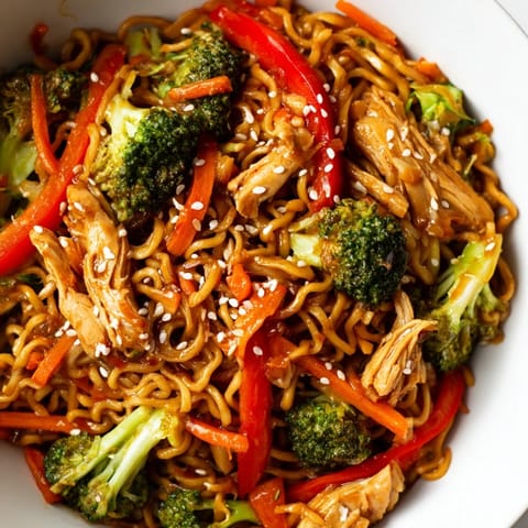 Steaming platter of homemade Spicy Ramen Stir-Fry, garnished with green onions and sesame seeds, served beside a cold lager.
