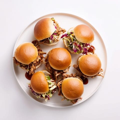 A close-up of juicy BBQ chicken sliders topped with creamy crunchy slaw on soft mini buns, ideal for easy weeknight dinners or parties.  