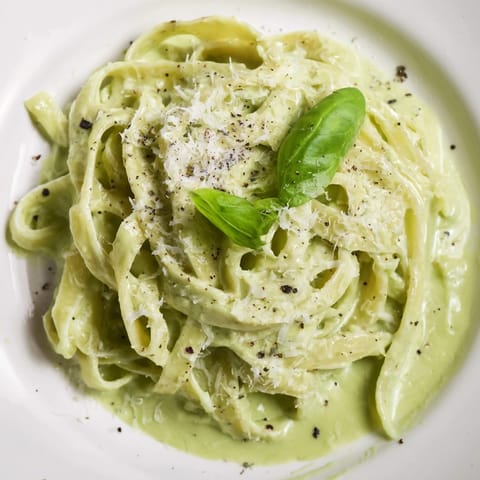 Steaming bowl of Creamy Green Pea Alfredo with grated Parmesan, paired with a crisp green salad.  