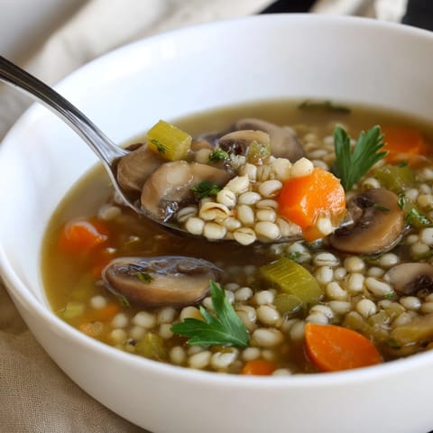 Steaming Mushroom and Barley Soup in a rustic bowl, topped with fresh parsley and a bright lemon wedge.