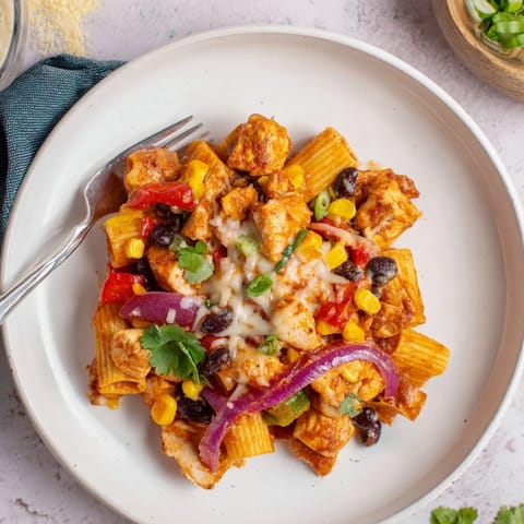 A close-up view of Crispy Chicken Burrito Pasta shows melted cheese, black beans, and corn, ready to serve with lime wedges.
