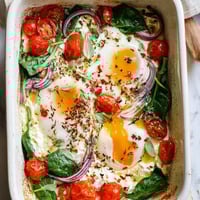 Baked Feta Eggs bubbling in a dish with roasted tomatoes, red onion, and herbs, perfect for breakfast.